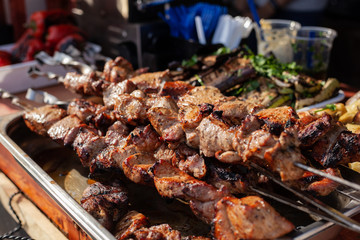 Roasted meat on a skew is on the table next to fried potatoes and vegetables in the open air