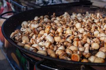 Lots of fried champignons in a large cast-iron skillet in the open air