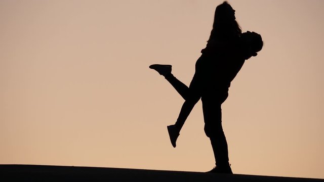 Cheerful young woman run to man and hug him. Guy lift girl up from ground, silhouetted shot of lovely couple meeting