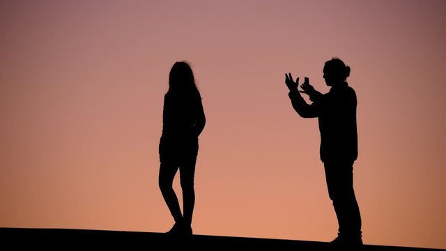 Couple in troubles, man say words and shake hands, woman stay back to him. Silhouetted shot of two people against clear sunset sky. Young lady turn around and make one gesture at the end of clip