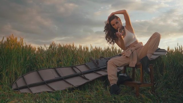 Pretty woman sitting in field with wings on her back and cigarette in her hands, resting after flight