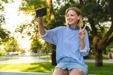 Image of woman taking selfie photo and gesturing peace sign