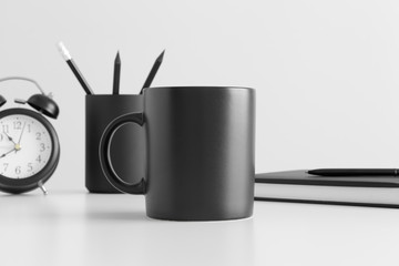 Black mug mockup with workspace accessories on a white table.