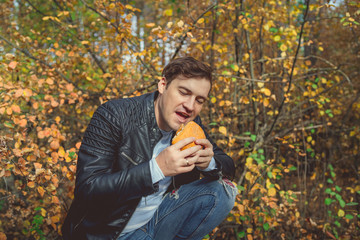 Man eating a Burger in a sunny spring park. Young male with Sunny day eating hamburger in autumn forest.