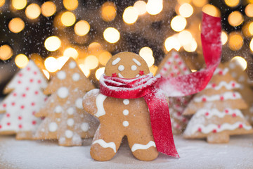 Fototapeta na wymiar smiling gingerbread man cookie in a red scarf with christmas trees cookies and christmas lights on a background