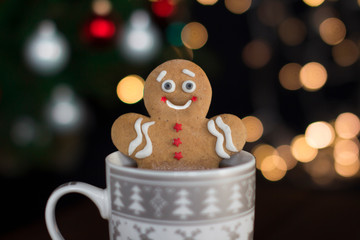 smiling gingerbread man cookie in a cup with hot drink with christmas lights on a background