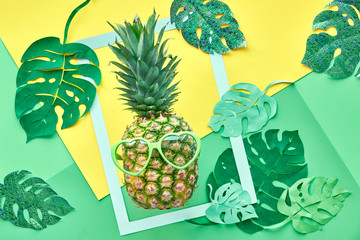 Funny pineapple in sunglasses, frame and paper exotic leaves in neo mint, green and yellow