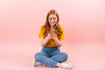 Cheerful girl isolated over pink wall background using mobile phone.