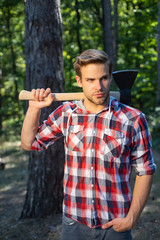 Obraz premium Stylish young man posing like lumberjack. The Lumberjack working in a forest. Handsome man with axe. Strong man lumberjack with an ax in a plaid shirt.