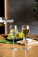Pouring white wine into the glass above the table set with grape cheese appetizers