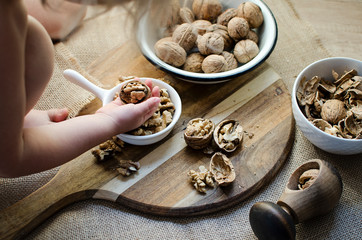 Walnuts in a hand of little girl, in the bowl and on wooden table. Fresh healthy snack food for vegetarian diet. Close up. 