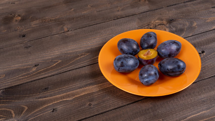 Plums on an orange plate on a wooden vintage table angled view