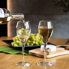 Pouring white wine into the glass above the table set with grape cheese appetizers
