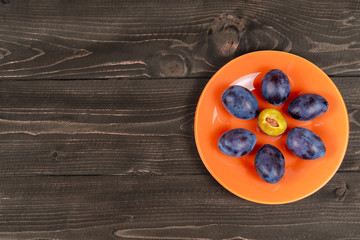 Plums on an orange plate on a wooden vintage table top view