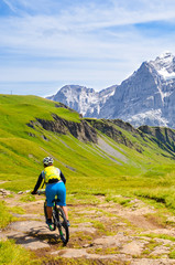 Fototapeta na wymiar Mountain biker riding downhill in the Swiss Alps. Famous mountains Jungfrau, Eiger and Monch in the background. Mountain biking, cycling in Switzerland. Cyclist with helmet. Active lifestyle concept