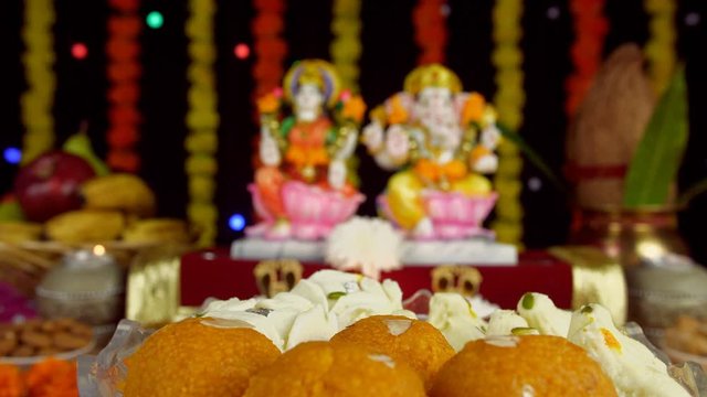 A tempting bowl of sweets for Diwali celebration with decorated blur temple in the background. A rotating bowl of delicious sweets like - Laddu  Modak  and Chamcham on the occasion of Diwali festival