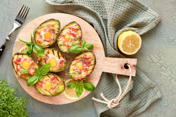 Top view on grilled avocado boats with bacon and quail eggs, flat lay on wooden background