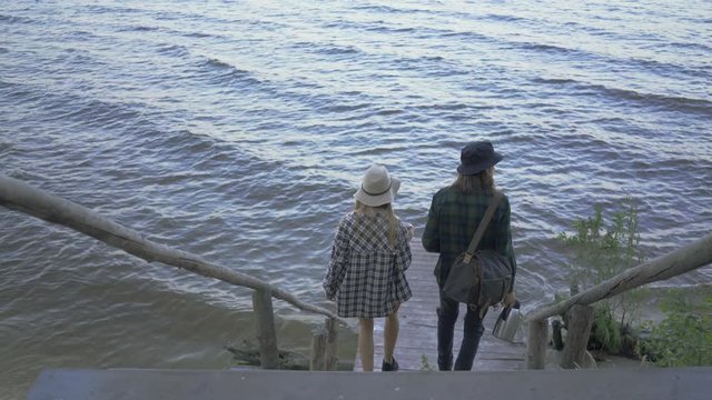Young caucasian couple walking down the stairs to the small pier. Friends spending time together outdoors
