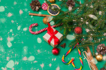 fir branches on a green background, a gift box with a red ribbon, cones, Golden and red balls, cinnamon sticks, candy,