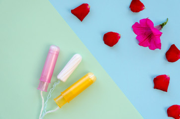 Three different tampons in front of a pink petunia flower and red rose petals. Hygiene products for women's monthly menstruation. Protection tampon for female health. Copy space. Top view. Flat lay