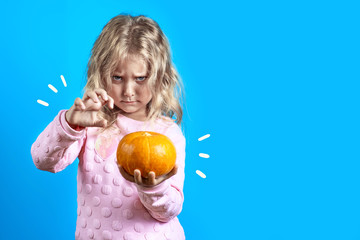 cute witch girl with blonde hair conjures over a pumpkin on colored background