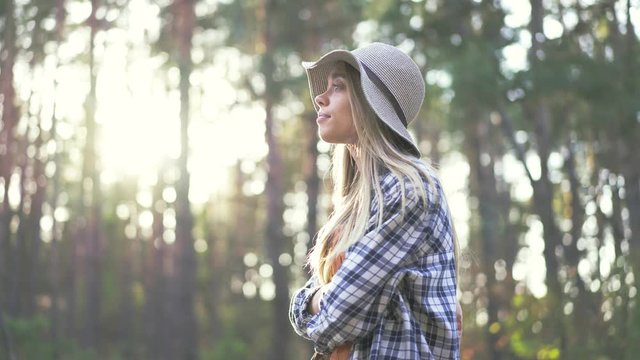 Young caucasian woman in plaid hipster shirt and straw hat trying to hitchhike the car near the forest