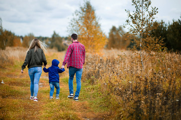 young parents walk with their little son on a country road, rear view. Copy space