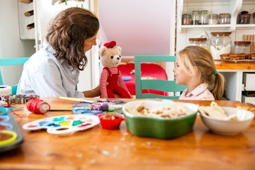 Mother and daughter playing with teddy bear in the kitchen