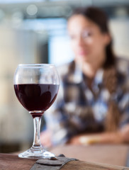 girl looking at glass of red wine standing on wooden barrel in winery