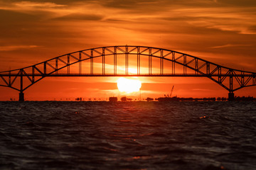 Steel tied arch bridge over water with a sunset behind it. Telephoto large sun - Fire Island Inlet Bridge, Long Island. 