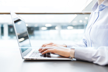 Young businesswoman using computer in office. Female hands typing on laptop keyboard. Blurred...