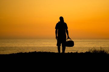 silhouette of a man wearing a beanie and holding a duffle bag summer travel concept