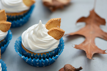 Close up autumn cupcakes decorated with cream and cookies leaves on gray wooden background. Soft focus. Thanksgiving day or Halloween celebration concept