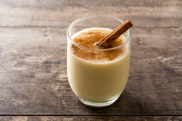 Homemade eggnog with cinnamon in glass on wooden table. Typical Christmas dessert.