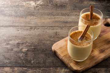 Homemade eggnog with cinnamon in glass on wooden table. Typical Christmas dessert.