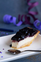 A slice of cheesecake on dark background with lilac serpentine. lifestyle photo of a piece of birthday cake, copy space