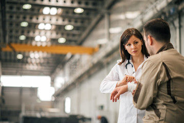 Female doctor treating manual worker at factory hall, copy space.