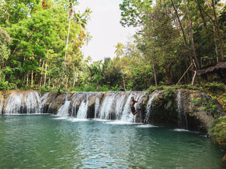 man swinging with the rope at the pool of waterfalls, Cambugahay Falls on Siquijor Island in...