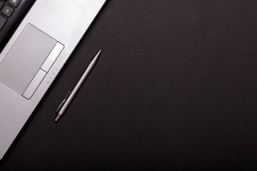 Minimal office desk or table with laptop and pen, with copy space. Top view or flat lay. Silver laptop with pen on black table.