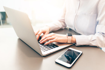 Young businesswoman using computer in office. Female hands typing on laptop keyboard. Blurred...