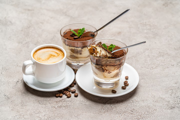 Portion of Classic tiramisu dessert in a glass and cup of coffee on concrete background