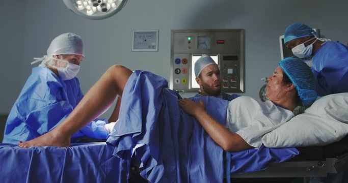 Side view of Caucasian female surgeon examining pregnant woman during labor in operation theater at 