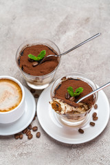 Portion of Classic tiramisu dessert in a glass and cup of coffee on concrete background