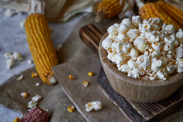 Traditional popcorn in a wooden bowl and corncobs on the table.