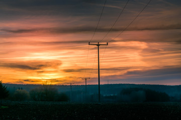 Colorful orange sunset over rolling rural hills with silhouetted poles in a scenic landscape in a...