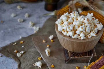 Traditional popcorn in a wooden bowl and corncobs on the table.
