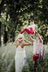 a father tosses a son, and a mother stands near among greenery lawn