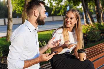 Fototapeta premium Young business colleagues man and woman talking with each other using mobile phones sit in nature park.