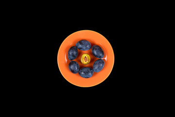 Fototapeta premium Plums on an orange plate isolated on a black background top view