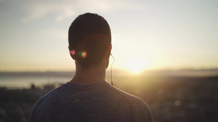 close up shot of rear view of a athletic fitness man with earphones in his ears looking at sunrise inspirational landscape - man admiring sunrise - Powered by Adobe